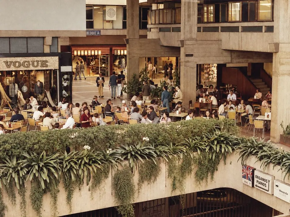 Recreación de una fotografía histórica: Terraza interior del centro comercial llena de gente en las mesas, 1977